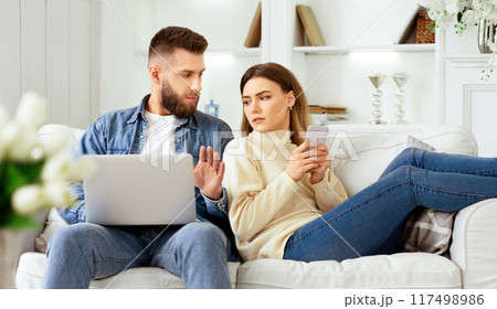 Woman Spying Husband's Laptop, Sitting Together On Sofa With Devices 117498986