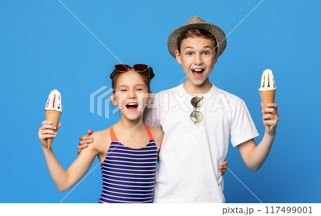 Happy little boy and girl embracing with ice cream cones, blue studio background Happy little boy and girl embracing with ice cream cones, blue studio background 117499001
