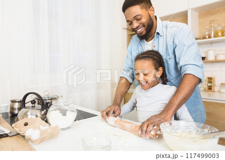 Smiling Black Man And His Daughter Rolling Dough Together At Kitchen, copy space 117499003