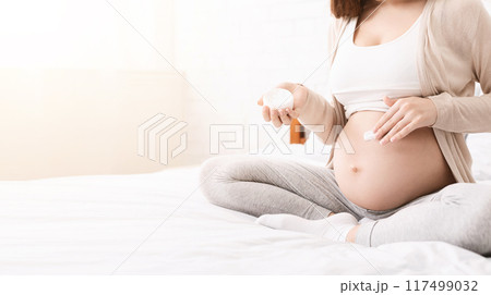 Close up of pregnant woman applying moisturizing cream on her belly, sitting on bed, panorama with empty space 117499032