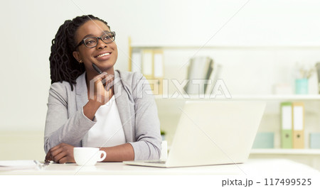 Dreamy African American businesswoman sitting at her office, working on laptop, looking at copy space, panorama 117499525