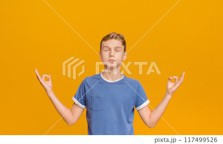 Zen, meditation, balance and peace concept. Portrait of cute little boy holding his fingers in mudra gesture, meditating with closed eyes, orange background Zen, meditation, balance and peace concept. Portrait of cute little boy holding his fingers in mudra gesture, meditating with closed eyes, orange background 117499526