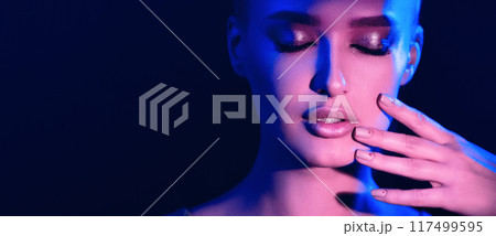 A woman closes her eyes and touches her face gently, bathed in dramatic blue and purple lighting, creating a contemplative mood, panorama with copy space A woman closes her eyes and touches her face gently, bathed in dramatic blue and purple lighting, creating a contemplative mood, panorama with copy space 117499595