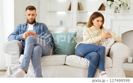 Family quarrel. Couple Staring At Their Own Smartphones, Sitting On Different Sides Of Couch Family quarrel. Couple Staring At Their Own Smartphones, Sitting On Different Sides Of Couch 117499599