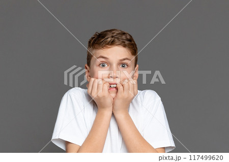 A teenage boy expressing surprise, hands on cheeks, isolated on a grey background. This image captures a youngster's candid reaction A teenage boy expressing surprise, hands on cheeks, isolated on a grey background. This image captures a youngster's candid reaction 117499620