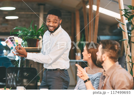 Colleagues discuss and review color swatches in a modern, daylight-filled office, engaging in a creative team meeting. Colleagues discuss and review color swatches in a modern, daylight-filled office, engaging in a creative team meeting. 117499693