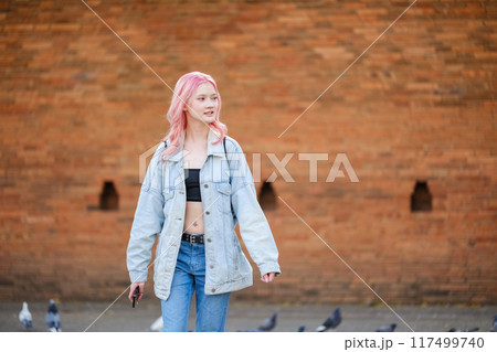 A woman with pink hair is walking down a brick wall 117499740