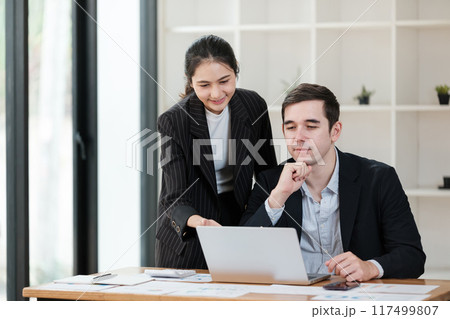 A woman and a man are sitting at a desk with a laptop in front of them A woman and a man are sitting at a desk with a laptop in front of them 117499807
