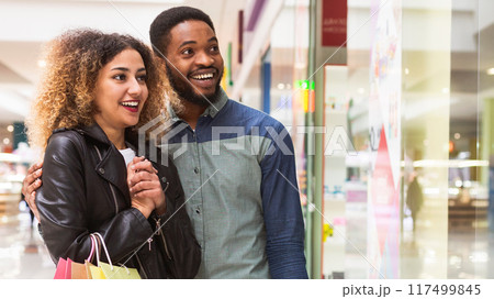 A joyful African American man and woman are strolling through a mall corridor, their expressions suggesting they just made some delightful purchases, copy space 117499845