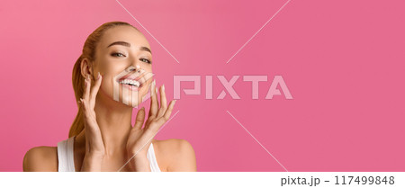 Portrait of beautiful woman touching skin or applying cream over pink background 117499848