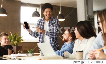 Look here. Guy showing phone to student friends, doing research in library together 117500061