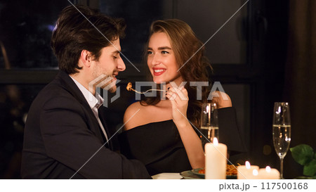 Romantic beautiful European couple having dinner in restaurant, feeding each other, enjoying delicious food Romantic beautiful European couple having dinner in restaurant, feeding each other, enjoying delicious food 117500168