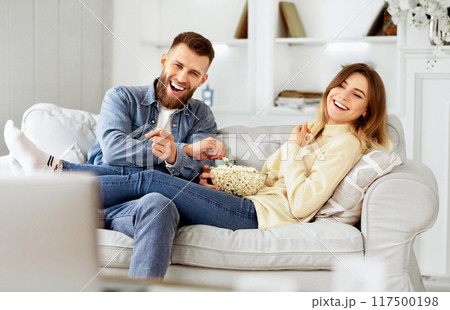 Young Couple Laughing Watching Comedy Movie Online And Eating Popcorn 117500198