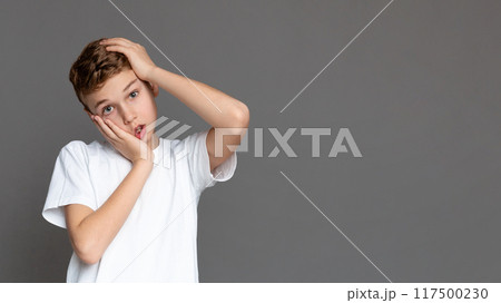 A contemplative teenager with a hand on his head, isolated on a gray background, suggesting thoughtfulness in a youngster A contemplative teenager with a hand on his head, isolated on a gray background, suggesting thoughtfulness in a youngster 117500230
