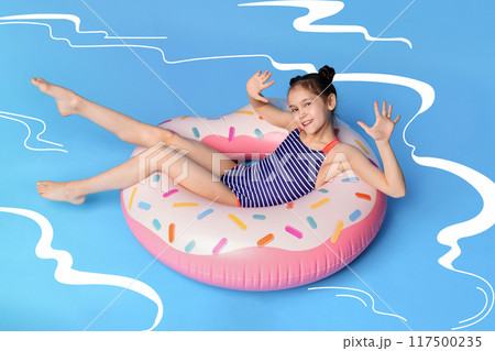 A young girl, wearing a swimsuit, is lying on an inflatable donut float in illustrated swimming pool. The girl seems relaxed and content as she floats on the colorful donut. A young girl, wearing a swimsuit, is lying on an inflatable donut float in illustrated swimming pool. The girl seems relaxed and content as she floats on the colorful donut. 117500235