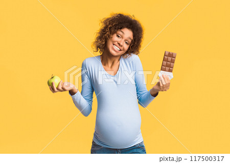 Pregnancy diet. Pregnant woman choosing between apple and chocolate over white background Pregnancy diet. Pregnant woman choosing between apple and chocolate over white background 117500317
