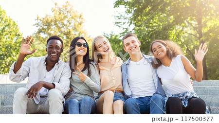 Happy friends international students spending time together in the summer city, sitting on stairs and smiling Happy friends international students spending time together in the summer city, sitting on stairs and smiling 117500377