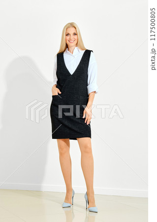 Smiling woman in white shirt and black sleeveless overknee dress posing Smiling woman in white shirt and black sleeveless overknee dress posing 117500805