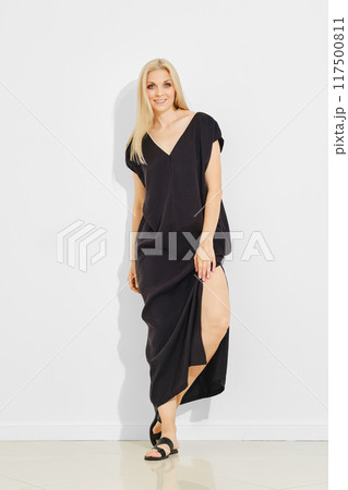 Playful woman in v neck sundress and sandals leaning against white wall Playful woman in v neck sundress and sandals leaning against white wall 117500811