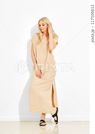 Sensual blonde woman in maxi sundress with short sleeves posing over white wall 117500812