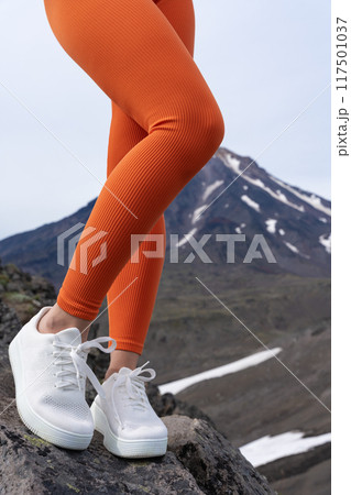 Woman is showing off her amazing fitness model legs in some orange sports leggings and sneakers. Sportsperson posing, enjoying outdoor fitness workout while hiking and trail running in mountains Woman is showing off her amazing fitness model legs in some orange sports leggings and sneakers. Sportsperson posing, enjoying outdoor fitness workout while hiking and trail running in mountains 117501037
