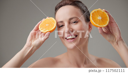 Beauty, health, cosmetics, anti-aging therapy and skin care concept - young beautiful brunette Caucasian woman holding half a orange, concept of freshness, vitamins and nutrients Beauty, health, cosmetics, anti-aging therapy and skin care concept - young beautiful brunette Caucasian woman holding half a orange, concept of freshness, vitamins and nutrients 117502111