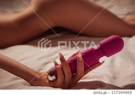 sex vibrator in hand of a woman girl with a sexy body in underwear lying on white sheet on bed in bedroom. Sex toys for female satisfaction and orgasm 117504909