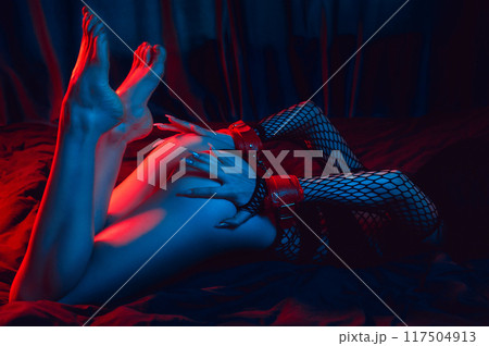 submissive woman with a sexy body and big booty with hands in BDSM handcuffs lies on bed in bedroom. Slave girl for sex with submission and domination 117504913