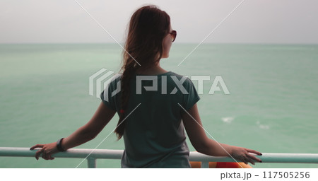 Woman strand on the boat deck looking on sea water. Sailing on the ferry boat. Long hair tourist girl in sunglasses. Outdoor lifestyle travel on summer holiday vacation. Back view, zoom in 117505256