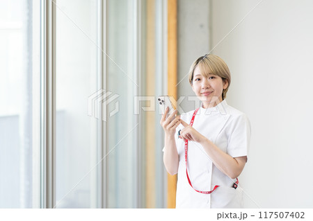 スマホを持つ金髪ショートヘアの若い女性看護師（髪色自由、自分らしく働く、職場環境） 117507402