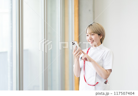 スマホを持つ金髪ショートヘアの若い女性看護師(髪色自由、自分らしく働く、職場環境) スマホを持つ金髪ショートヘアの若い女性看護師(髪色自由、自分らしく働く、職場環境) 117507404