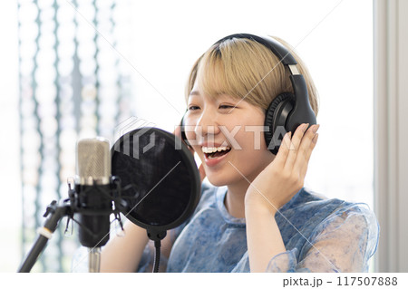 歌を歌う金髪ショートヘアの若い女性(コンデンサーマイク、録音、ボーカル、ナレーター) 歌を歌う金髪ショートヘアの若い女性(コンデンサーマイク、録音、ボーカル、ナレーター) 117507888