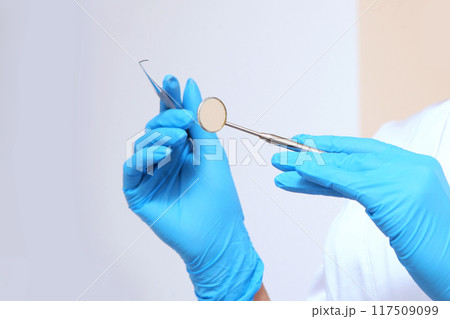 A gloved hand holds professional dental instruments. Dental mirror in the hands of a doctor for examination. 117509099