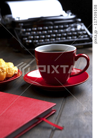 A red cup with coffee. An old vintage typewriter and an empty piece of paper. The notebook is red. The concept of a business breakfast. 117509108