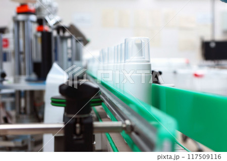 A white plastic bottle is moving along a conveyor belt. Production of cosmetics and skin care products. A capping and labeling machine. 117509116