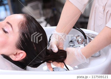 In beauty salon, strengthening mask is applied to hair. Wet hair. Mask for moisturizing hair.Long hair is washed and moisturized with cosmetic mask. In beauty salon, strengthening mask is applied to hair. Wet hair. Mask for moisturizing hair.Long hair is washed and moisturized with cosmetic mask. 117509121