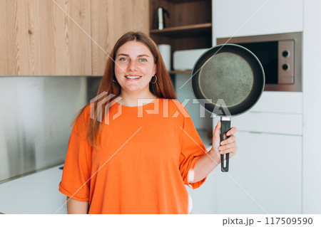 Young woman housewife holding empty pan in the kitchen at home. Domestic life and diet concept. Food banner. Time to eat 117509590