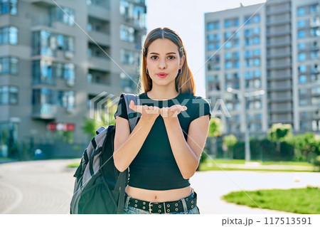 Happy young teenage female with red hair backpack making air kiss gesture Happy young teenage female with red hair backpack making air kiss gesture 117513591