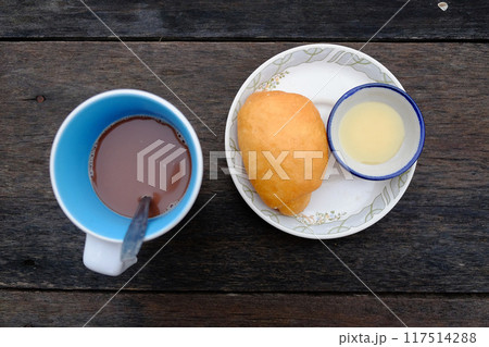 Yang fried dumpling or Bread fried bun recipe with sweetened condensed milk in a bowl and a cup of hot chocolate on wooden table in tropical garden. Asain Breakfast in Thailand Yang fried dumpling or Bread fried bun recipe with sweetened condensed milk in a bowl and a cup of hot chocolate on wooden table in tropical garden. Asain Breakfast in Thailand 117514288