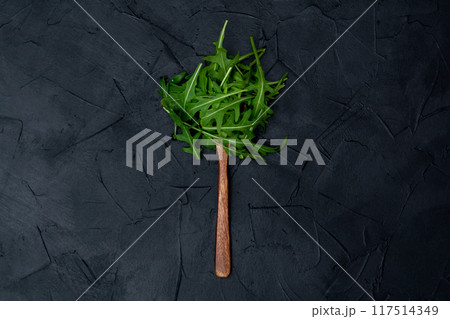 Fresh arugula leaves on a wooden spoon on a black background Fresh arugula leaves on a wooden spoon on a black background 117514349