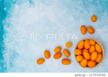 Kumquat in a wooden bowl on a blue background. Kumquat in a wooden bowl on a blue background. 117514350