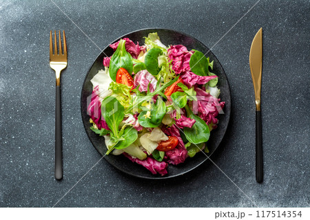 Salad with cabbage, radicchio and tomatoes in black plate on dark background 117514354
