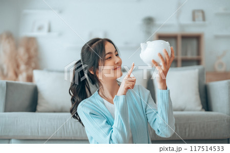 Young Asian woman holding piggy bank and sitting on the floor at home 117514533