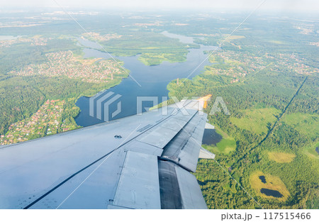 View of airplane wing, blue skies and green land during landing. Airplane window view. View of airplane wing, blue skies and green land during landing. Airplane window view. 117515466