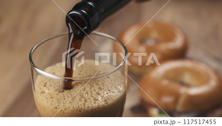 stout beer poring into glass with bagels on background 117517455
