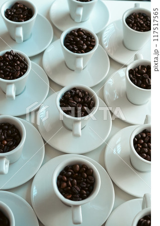 テーブルに並べられたコーヒー豆が入っている白いコーヒーカップとソーサー 縦素材 テーブルに並べられたコーヒー豆が入っている白いコーヒーカップとソーサー 縦素材 117517565