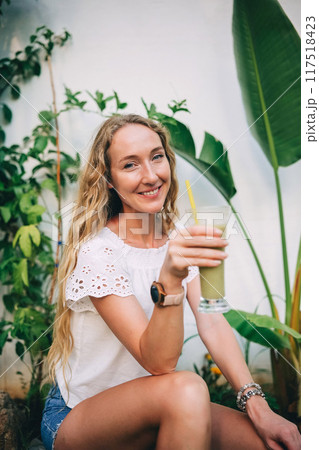 Woman enjoying a green smoothie in a tropical garden during a sunny day Woman enjoying a green smoothie in a tropical garden during a sunny day 117518423