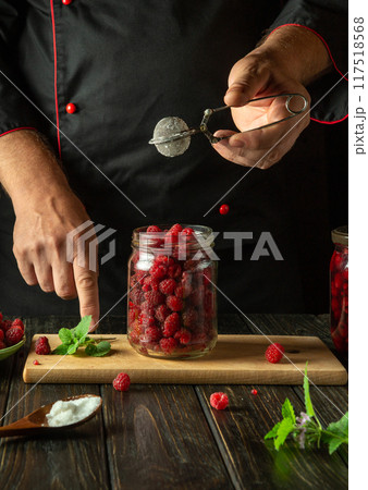 Chef preserves red raspberry in a jar. Concept of cooking sweet jam with sugar on the kitchen table. Adding citric acid to raspberries Chef preserves red raspberry in a jar. Concept of cooking sweet jam with sugar on the kitchen table. Adding citric acid to raspberries 117518568
