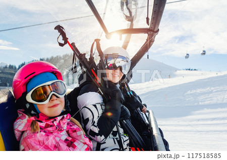 Cute little girl with mom in helmet and goggles having fun sitting on ski lift chair enjoying winter ski vacations in alpine austrian mountains. Happy family portrait winter sport holidays Cute little girl with mom in helmet and goggles having fun sitting on ski lift chair enjoying winter ski vacations in alpine austrian mountains. Happy family portrait winter sport holidays 117518585