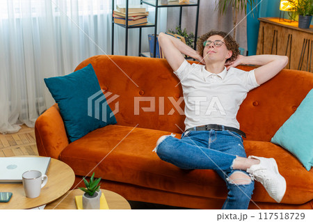 Tired young man in glasses sitting on comfortable couch, taking a rest daytime nap resting at home Tired young man in glasses sitting on comfortable couch, taking a rest daytime nap resting at home 117518729